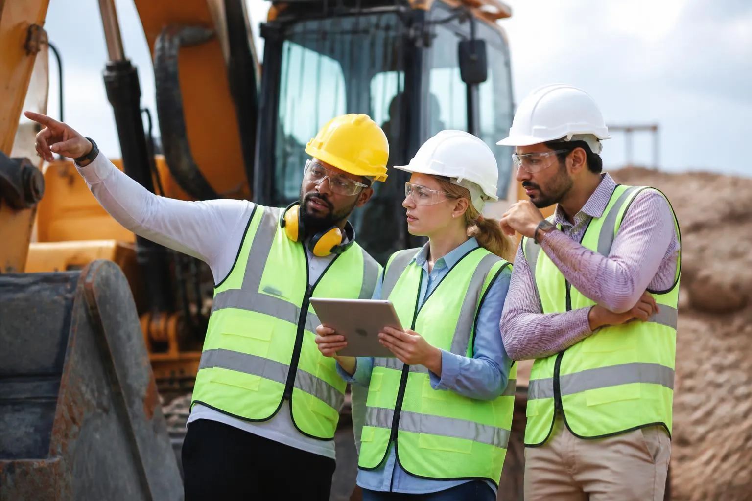 Sahada iş makinasının yanında teknik çizimleri inceleyen mühendisler